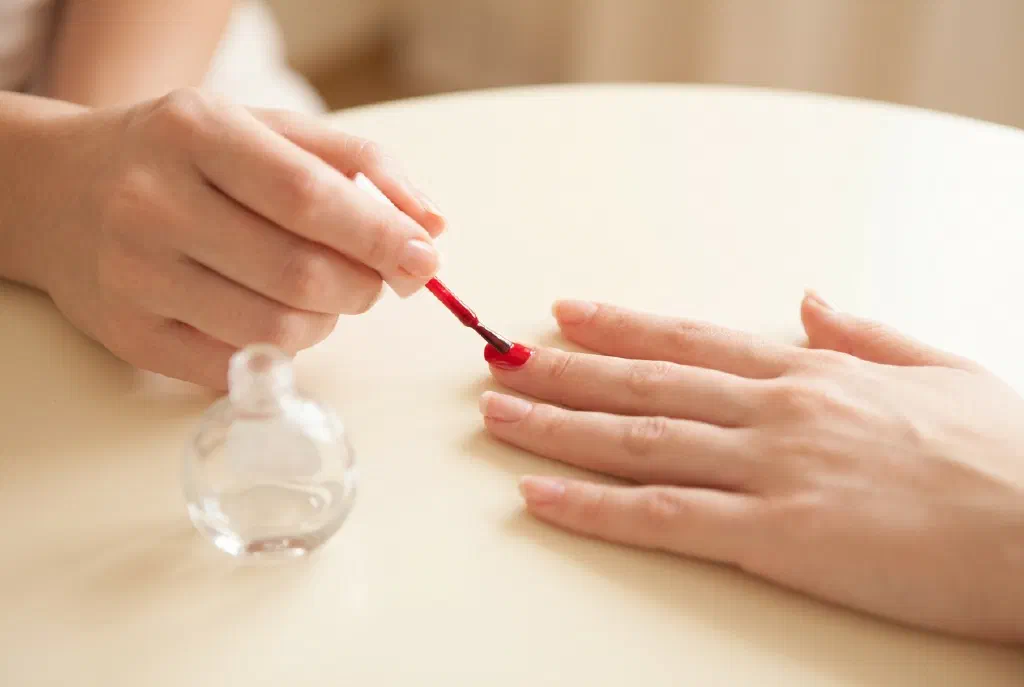 Bàn tay sơn lớp sơn móng đỏ mỏng lên những móng tay được chăm sóc kỹ