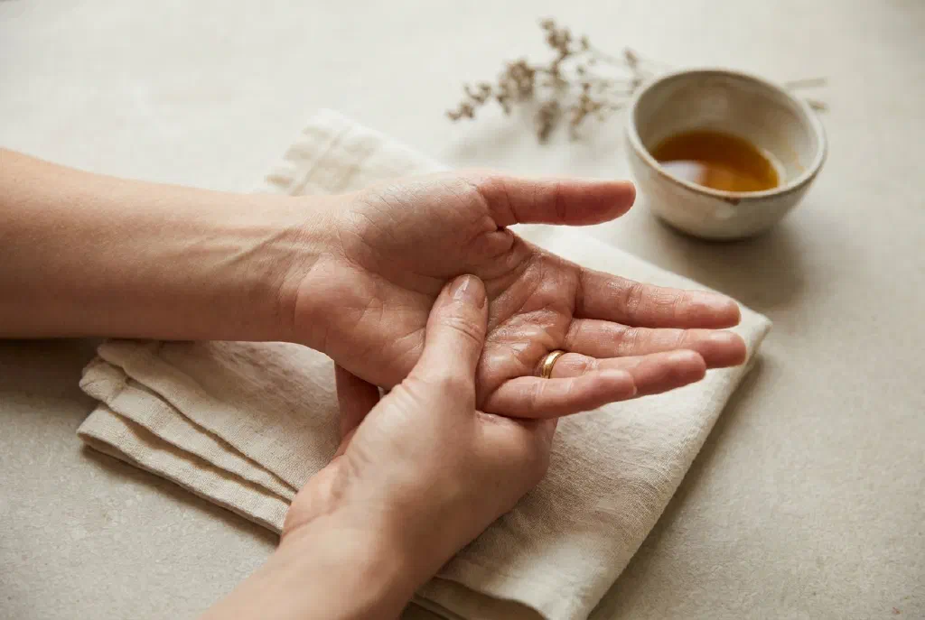 Zwei Hände, die sich gegenseitig mit Massageöl die Handfläche massieren